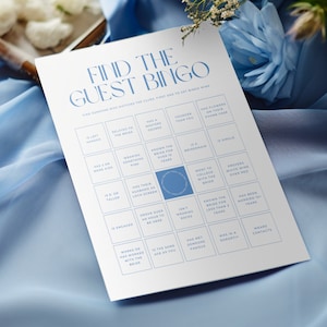 Puede incluir: Una tarjeta de bingo de boda azul y blanca con el título "Find the Guest Bingo". La tarjeta tiene una cuadrícula de 25 casillas con diferentes indicaciones para que los invitados puedan encontrar en la boda. Algunas de las indicaciones incluyen "Es zurdo", "Está relacionado con la novia", "Tiene un máster", "Conoce a la novia desde hace más de 10 años", "Es una dama de honor", "Es soltero", "Fue a la universidad con la novia", "Prefiere el vino blanco al vino tinto", "Conoce a la novia desde hace menos de 2 años", "Ha estado casado más de 10 años", "Trabaja o ha trabajado con la novia", "Tiene la misma edad que tú", "Ha conocido a alguien famoso", "Estuvo en una hermandad", "Usa lentes de contacto".