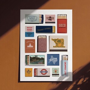 May include: A selection of matchboxes featuring diverse designs and text, including "Lady Bird," "Deep Eddy Cabaret," and "Austin." The matchboxes are in various colours, such as blue, red, and yellow, and are displayed on a white surface.