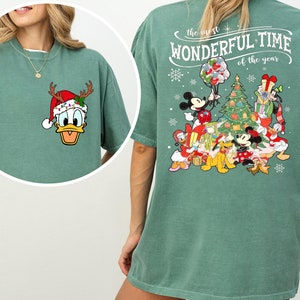 Puede incluir: Camiseta verde claro con un &aacute;rbol de Navidad y personajes de Mickey Mouse en la espalda. La parte delantera de la camiseta presenta una imagen de dibujos animados de Donald Duck con un gorro de Pap&aacute; Noel y cuernos de reno. El texto en la parte posterior dice "the most WONDERFUL TIME of the year".