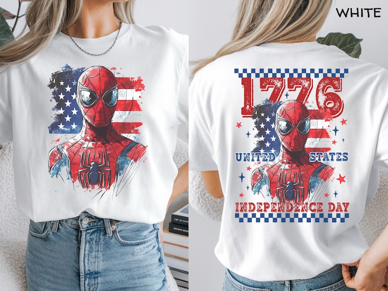 May include: A white t-shirt featuring a graphic of a red and blue superhero mask over a stylized American flag. The back design includes the text 1776, UNITED STATES, and INDEPENDENCE DAY, framed by a blue and white checkered border and red stars.