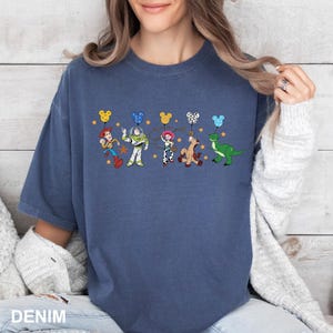 K&ouml;nnte beinhalten: Ein marineblaues T-Shirt mit einem Aufdruck der Toy Story-Charaktere, die Ballons halten. Zu den Charakteren geh&ouml;ren Woody, Buzz Lightyear, Jessie, Bullseye und Rex. Die Ballons sind in verschiedenen Farben, darunter Gelb, Rot, Blau und Gr&uuml;n.