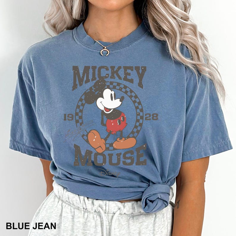 May include: A blue t-shirt featuring a vintage Mickey Mouse graphic. The graphic shows Mickey Mouse in a red and yellow outfit, with the text "Mickey Mouse" and "1928" surrounding him.