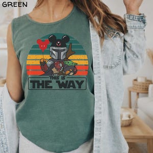 May include: Light green tank top featuring a graphic of a Mandalorian character with Mickey Mouse ears, holding a red heart balloon and Grogu. The design is set against a sunset background with the text "THIS IS THE WAY".