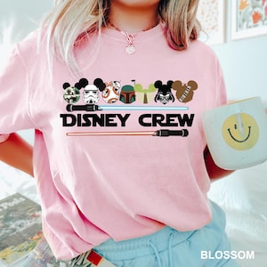 Pu&ograve; includere: Maglietta rosa con una grafica di vari personaggi Disney che indossano le orecchie di Topolino e il testo "DISNEY CREW".