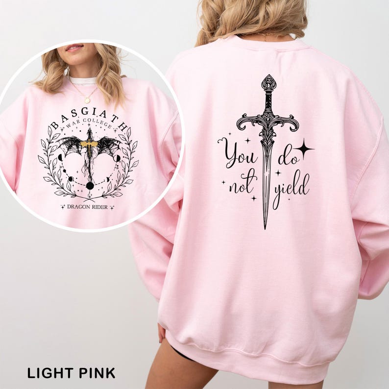 May include: Light pink sweatshirt with a black graphic on the front that says "BASGIATH WAR COLLEGE" with a dragon and sword design. The back of the sweatshirt has a sword graphic and the words "You do not yield".