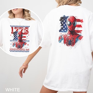 May include: A white t-shirt featuring a graphic of a superhero in a red and blue suit. The back design shows the superhero against an American flag background. The front design includes the text 1776 UNITED STATES INDEPENDENCE DAY.
