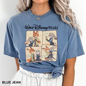 以下が含まれることがあります： ズートピアのキャラクターのグラフィックが特徴のブルージーンズカラーのTシャツ。「ウォルト・ディズニー・ワールド」の文字と、ニック・ワイルドとジュディ・ホップスの画像が4つのパネルに描かれています。快適でカジュアルなスタイルです。