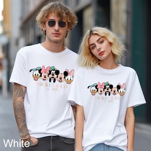 May include: Two white t-shirts with a graphic print of Mickey Mouse and friends. The text on the shirts reads "Mickey & Co. Est. 1928".