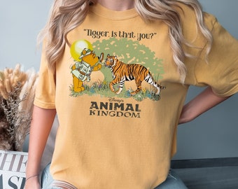 May include: A yellow t-shirt with a vintage-style graphic of Winnie the Pooh looking through a magnifying glass at Tigger. The text "Tigger. Is that you?" is above the image. Below the image is the text "Disney's Animal Kingdom".