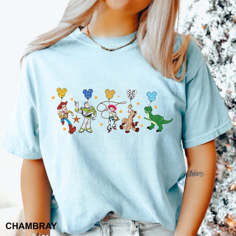 K&ouml;nnte beinhalten: Ein hellblaues T-Shirt mit einem Aufdruck von Toy Story-Charakteren, die Mickey-Maus-Ballons halten. Die Charaktere sind Woody, Buzz Lightyear, Jessie, Bullseye und Rex.