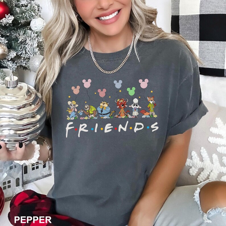 May include: Dark grey t-shirt with cartoon characters and the word "FRIENDS" in white. The design includes colourful balloons and the characters are holding. The shirt is a comfortable, casual style.
