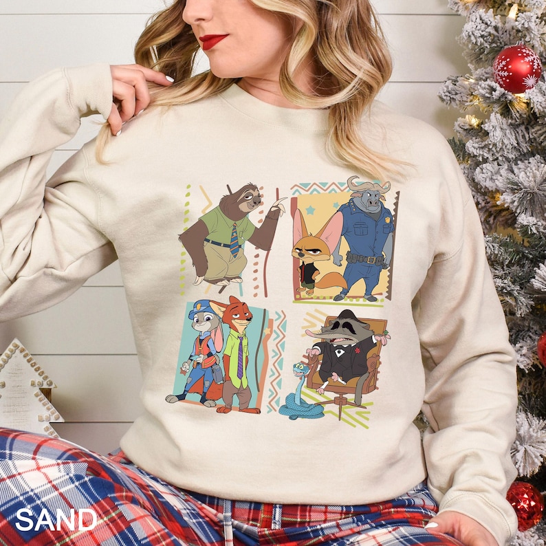 May include: Sand-colored sweatshirt featuring a colorful graphic of characters from the animated movie Zootopia. The design includes a sloth, fox, buffalo, rabbit, and raccoon. The sweatshirt has long sleeves and a crew neck.