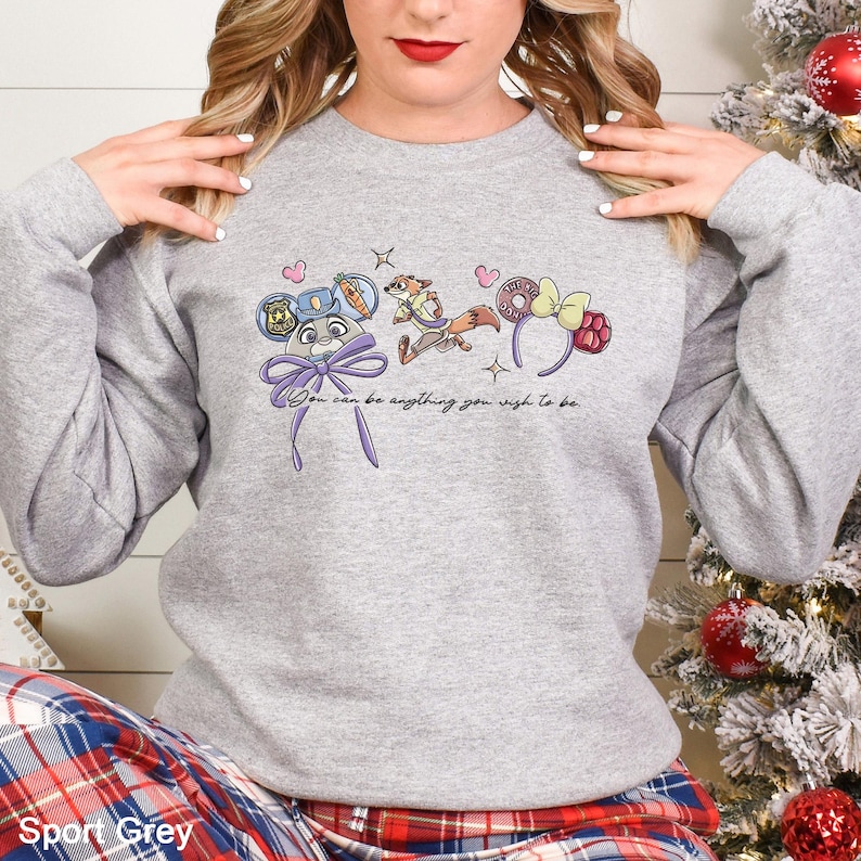 May include: Sport Grey sweatshirt featuring a whimsical design with cartoon characters and the text "You can be anything you wish to be." The design includes a mouse-eared hat, a fox, and a bow. The sweatshirt is a comfortable, casual style.