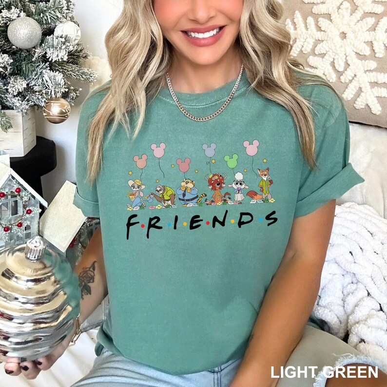 May include: Light green t-shirt with cartoon animal characters and the word "FRIENDS" in black. The shirt has rolled-up sleeves and a relaxed fit. The text "LIGHT GREEN" is at the bottom right. The design includes balloons.