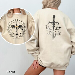 May include: Sand-colored sweatshirt with a black graphic on the front that says "BASGIATH WAR COLLEGE" and "DRAGON RIDER". The back features a sword design with the words "You do not yield".