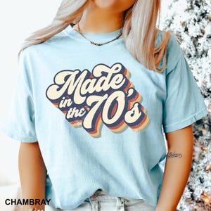 Puede incluir: Una camiseta azul claro con un gr&aacute;fico de estilo retro que dice "Made in the 70's".