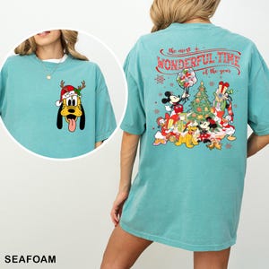 Puede incluir: Una camiseta azul turquesa con un dise&ntilde;o navide&ntilde;o con Mickey Mouse y sus amigos. La parte posterior de la camiseta dice "The most wonderful time of the year".