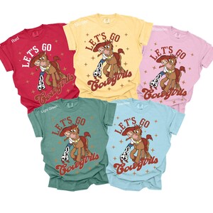 May include: Five t-shirts in different colours with the text "Let's Go Cowgirls" and a cartoon image of a horse and a girl riding the horse. The shirts are in the colours red, light green, butter, blossom, and light blue.