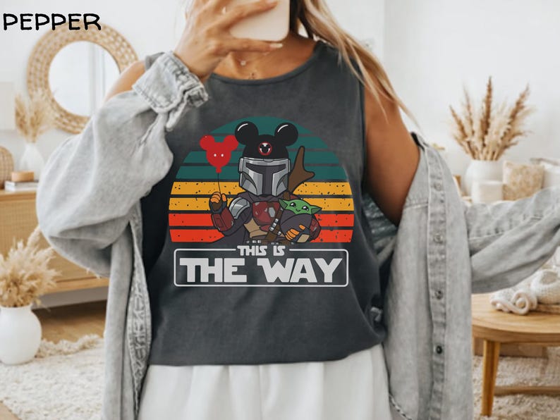 May include: Dark gray tank top featuring a graphic of a Mandalorian character with Mickey Mouse ears holding a heart-shaped balloon and Grogu. The design is set against a sunset background with the text "THIS IS THE WAY" in a white box.