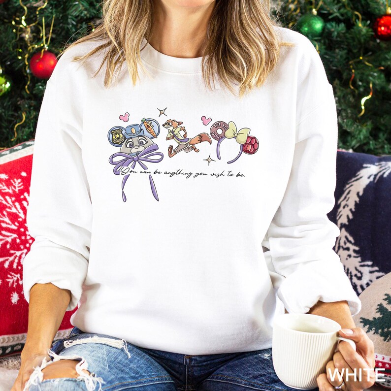 May include: White sweatshirt with a colorful graphic featuring cartoon characters and the text "You can be anything you wish to be." The design includes a bow, hearts, and stars. The sweatshirt is a casual, comfortable style.