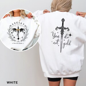 May include: White sweatshirt with a black graphic on the front and back. The front graphic says "BASGIATH WAR COLLEGE" with a dragon and sword design. The back graphic features a sword and the text "You do not yield."