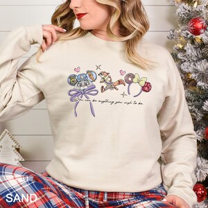 May include: Sand-colored sweatshirt featuring cartoon character designs and the text "You can be anything you wish to be." The design includes a police badge, a fox, and a bow. The sweatshirt has long sleeves.