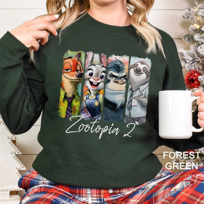 May include: Forest green sweatshirt featuring characters from Zootopia 2. The design includes Nick Wilde, Judy Hopps, a gorilla, and Flash the sloth. The text "Zootopia 2" is written in white script.