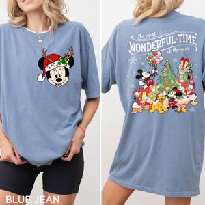 Puede incluir: Una camiseta azul con un dise&ntilde;o navide&ntilde;o con Mickey Mouse y otros personajes de Disney. El texto en la parte posterior de la camiseta dice "The most wonderful time of the year".