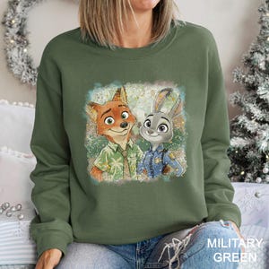 Pode incluir: Um moletom verde-oliva com um gr&aacute;fico colorido de Nick Wilde e Judy Hopps de Zootopia. O gr&aacute;fico est&aacute; em um fundo desbotado. O texto "MILITARY GREEN" est&aacute; impresso no canto inferior direito. O moletom &eacute; de gola redonda.