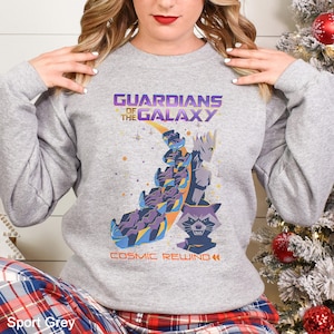 May include: Sport grey sweatshirt featuring a graphic of characters from Guardians of the Galaxy. The design includes the text "GUARDIANS OF THE GALAXY" and "COSMIC REWIND" in purple and yellow. The sweatshirt is a crew neck style.