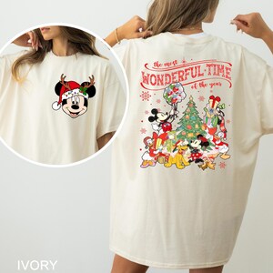 Puede incluir: Una camiseta blanca con un dise&ntilde;o navide&ntilde;o con Mickey Mouse y otros personajes de Disney. La parte delantera de la camiseta tiene una imagen de dibujos animados de Mickey Mouse con un gorro de Pap&aacute; Noel. La parte trasera de la camiseta tiene un dise&ntilde;o que dice "La &eacute;poca m&aacute;s maravillosa del a&ntilde;o" con Mickey Mouse, Minnie Mouse, Donald Duck, Goofy, Pluto y otros personajes reunidos alrededor de un &aacute;rbol de Navidad.