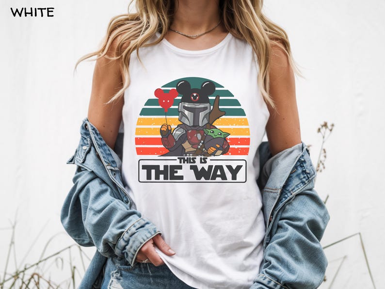 May include: White tank top featuring a graphic of a Mandalorian-inspired character with a Mickey Mouse head, holding a heart-shaped balloon, and Grogu. The design is set against a sunset backdrop with the text "THIS IS THE WAY".