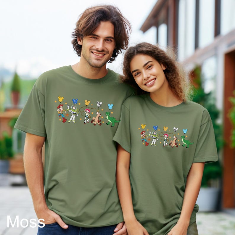 K&ouml;nnte beinhalten: Zwei Personen tragen gr&uuml;ne T-Shirts mit einem Aufdruck von Toy Story-Charakteren, die Ballons halten. Zu den Charakteren geh&ouml;ren Woody, Buzz Lightyear, Jessie, Bullseye und Rex.
