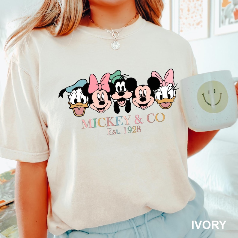 May include: A white t-shirt with a graphic of Mickey Mouse and friends. The graphic is in pastel colors and says "Mickey & Co. Est. 1928".