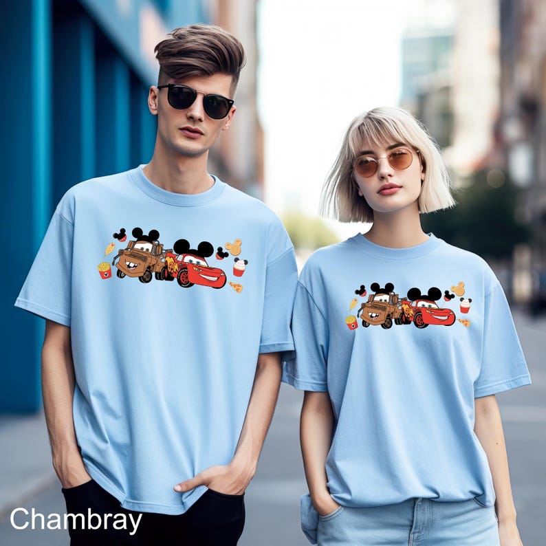 May include: Two light blue t-shirts with a graphic print of the characters Lightning McQueen and Mater from the Disney Pixar movie Cars. The graphic also includes Mickey Mouse ears and other details.