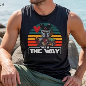 May include: Black sleeveless shirt featuring a graphic of a Mandalorian-themed Mickey Mouse holding a red heart balloon, with Grogu. The text "THIS IS THE WAY" is displayed below the graphic, set against a sunset background.