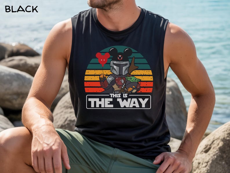 May include: Black sleeveless shirt featuring a graphic of a Mandalorian-themed Mickey Mouse holding a red heart balloon, with Grogu. The text "THIS IS THE WAY" is displayed below the graphic, set against a sunset background.