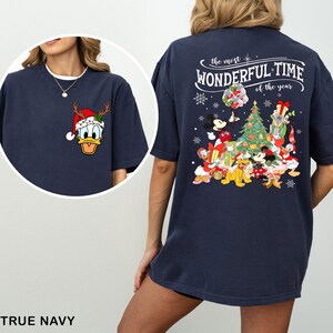 Puede incluir: Una camiseta azul marino con un dise&ntilde;o navide&ntilde;o con Mickey Mouse, Donald Duck y otros personajes de Disney reunidos alrededor de un &aacute;rbol de Navidad. El texto en la parte posterior de la camiseta dice "the most WONDERFUL TIME of the year".