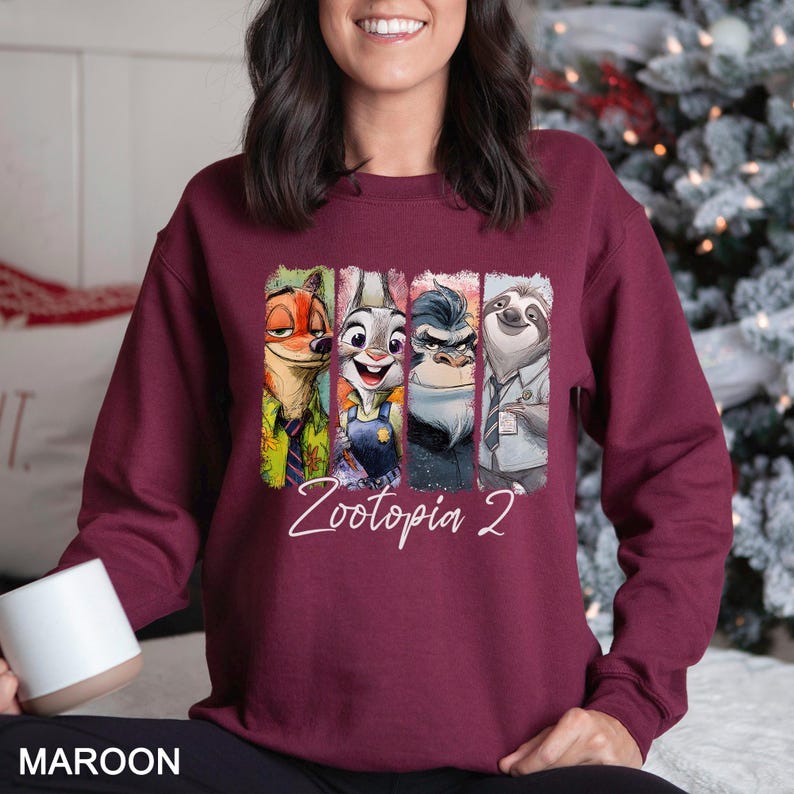 May include: Maroon sweatshirt featuring characters from Zootopia. The design includes Nick Wilde, Judy Hopps, a rhino, and Flash the sloth. The text "Zootopia 2" is written in white script. The word "MAROON" is printed at the bottom.