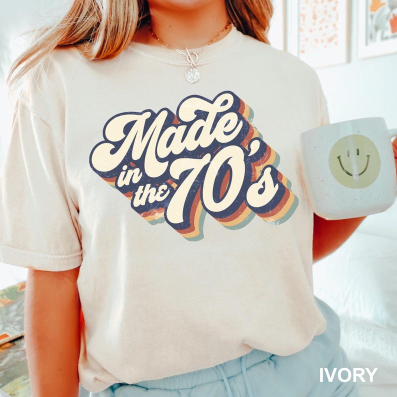 Puede incluir: Una camiseta blanca con un gr&aacute;fico de estilo retro que dice "Made in the 70's" en colores arco&iacute;ris.