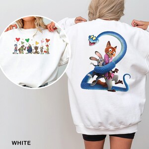 May include: White sweatshirt featuring a colorful cartoon design on the front and back. The front design includes cartoon characters with heart-shaped balloons. The back design features a blue snake with cartoon characters.