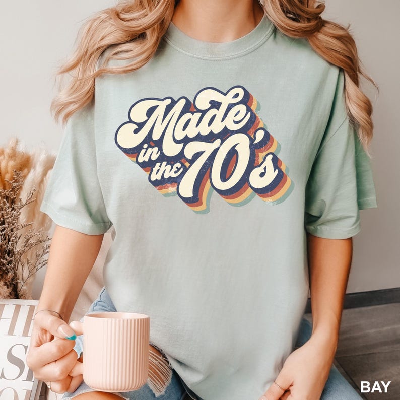 Puede incluir: Una camiseta azul claro con un gr&aacute;fico de estilo retro que dice "Made in the 70's" en letras coloridas con forma de arco&iacute;ris.
