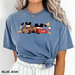 May include: A blue t-shirt with a graphic of Mickey Mouse, Mater from Cars, and Lightning McQueen from Cars. The graphic also includes Mickey Mouse ears, a cupcake, pizza, and french fries.