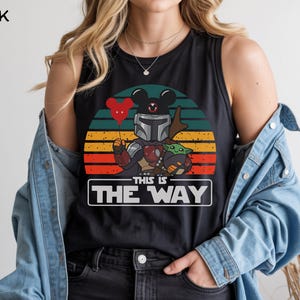 May include: Black tank top featuring a graphic of The Mandalorian and Grogu with a Mickey Mouse head balloon against a sunset backdrop. The text "THIS IS THE WAY" is displayed in a white rectangle.