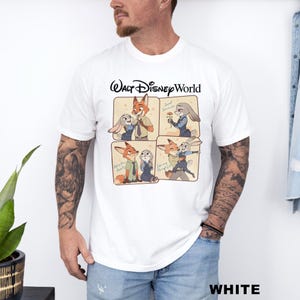 以下が含まれることがあります： 白のTシャツ。映画「ズートピア」のニック・ワイルドとジュディ・ホップスの漫画デザインが特徴です。「Walt Disney World」の文字が漫画の画像の上にあります。「WHITE」の文字がシャツの下部に太字で印刷されています。