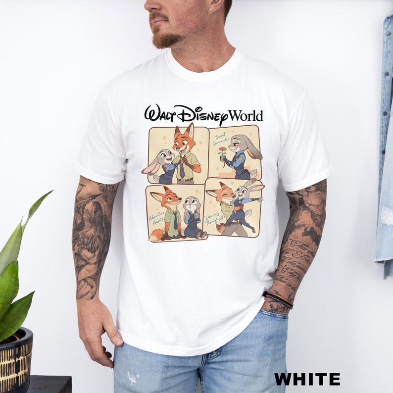 以下が含まれることがあります： 白のTシャツ。映画「ズートピア」のニック・ワイルドとジュディ・ホップスの漫画デザインが特徴です。「Walt Disney World」の文字が漫画の画像の上にあります。「WHITE」の文字がシャツの下部に太字で印刷されています。