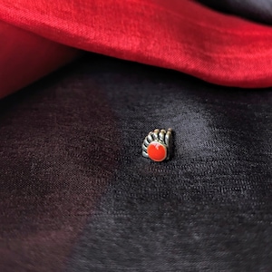 Op de afbeelding: Een zilveren neusring met een rode edelsteen. De ring ligt op een zwarte stoffen achtergrond.