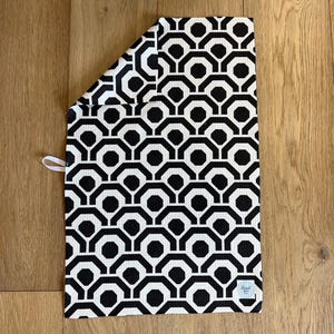 May include: Black and white kitchen towel with a geometric pattern. The towel has a black border and a white label with the text "Elegant Home" in black.