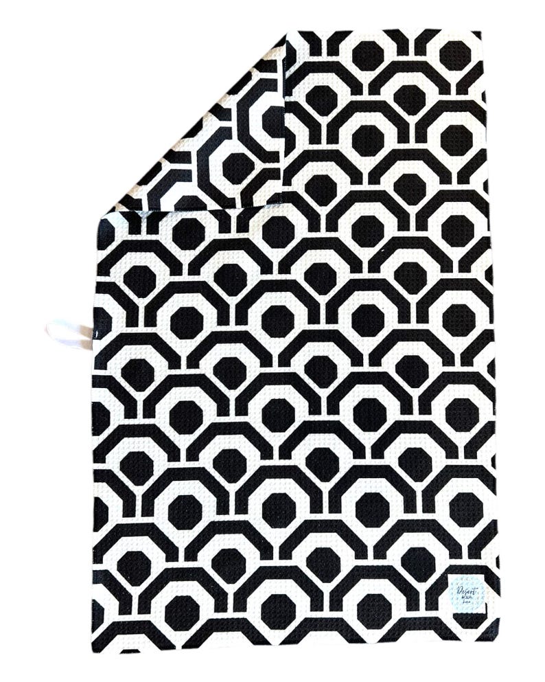 May include: Black and white geometric patterned kitchen towel with a small white tag that says "Design by"