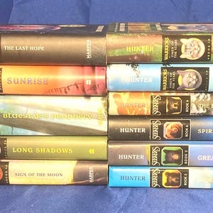 K&ouml;nnte beinhalten: Ein Stapel von B&uuml;chern der "Warriors"-Reihe von Hunter. Die Buchr&uuml;cken zeigen Titel wie "The Last Hope" und "Sunrise". Die farbenfrohen Cover zeigen Illustrationen von Katzen und Landschaften. Die B&uuml;cher sind gestapelt.